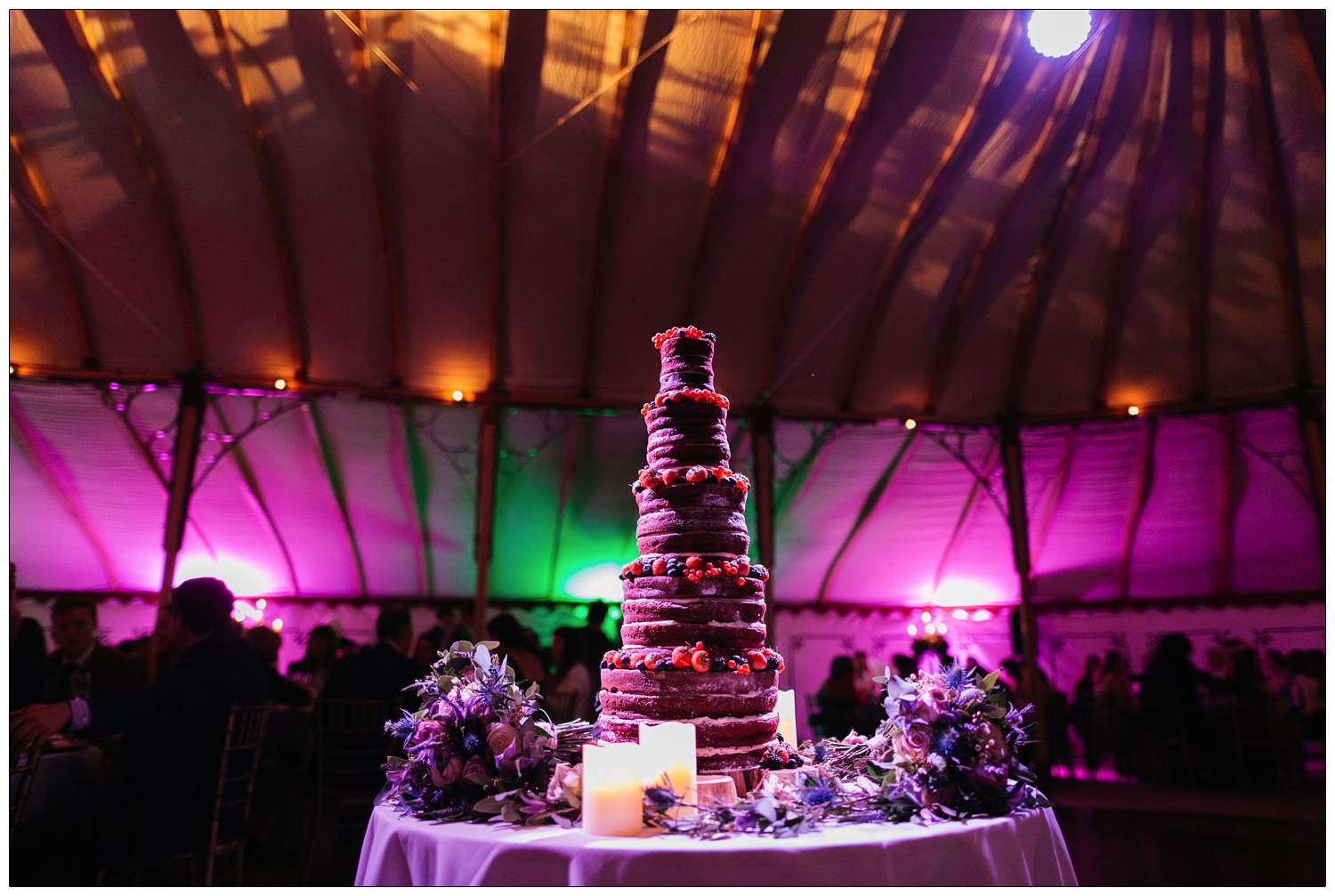 A really tall rustic style wedding cake under magenta lights.