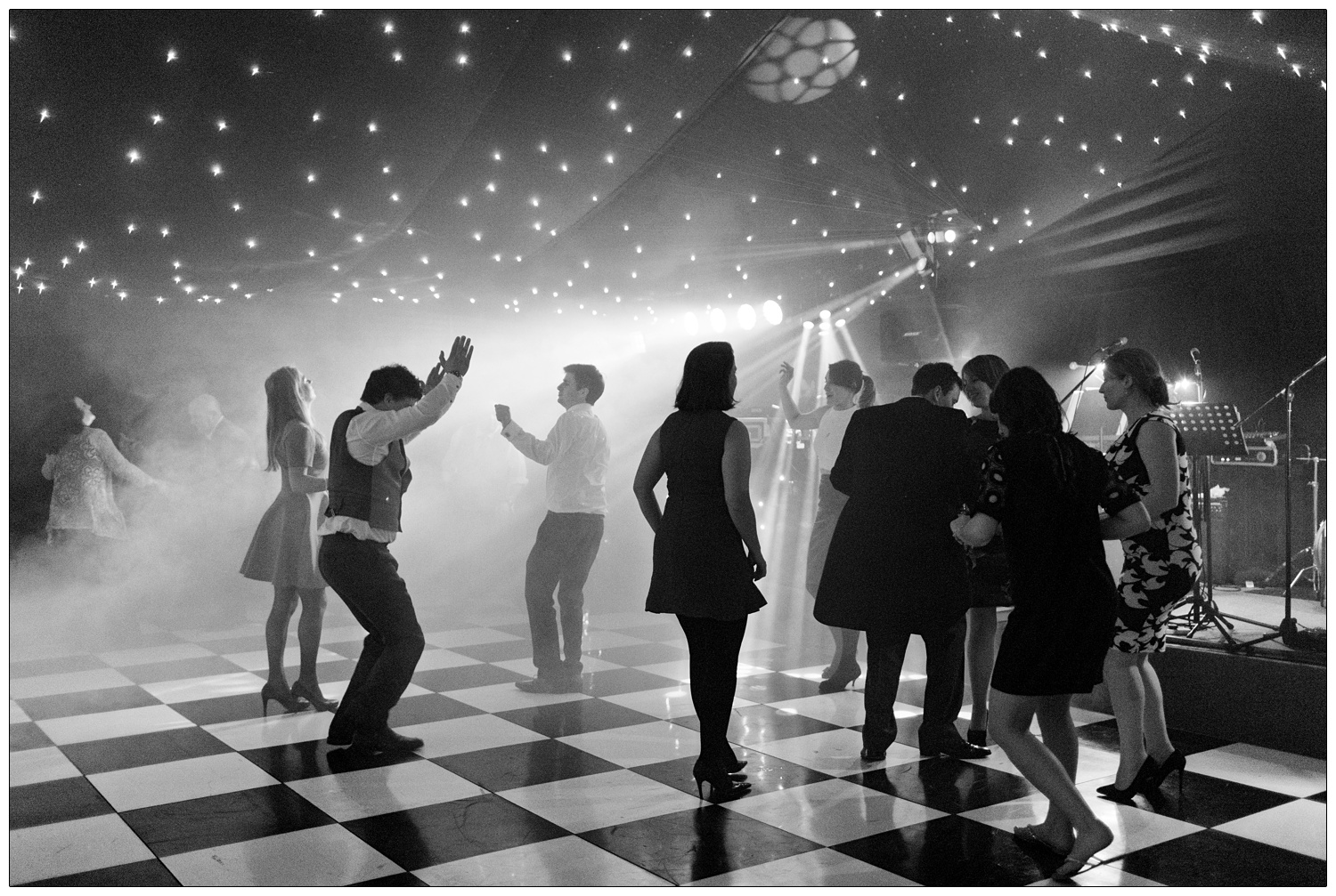 People dance on a black and white chequered at a wedding.