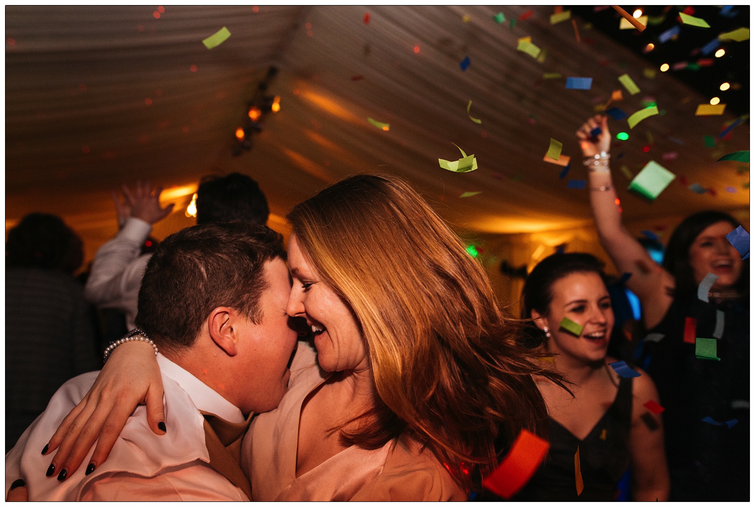 A man and woman dance together as coloured confetti falls from the air at a wedding reception.