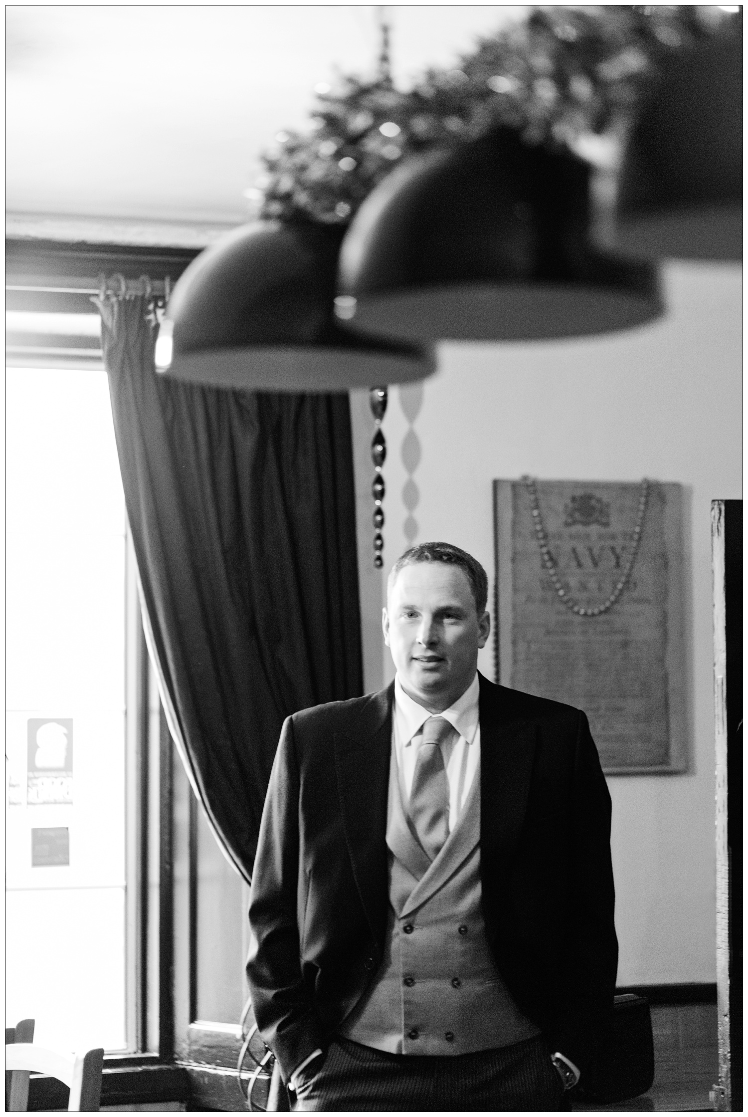 The groom stands in The Green Man Inn in Bradwell-on-Sea. He is wearing a morning suit with his hands in his pockets.