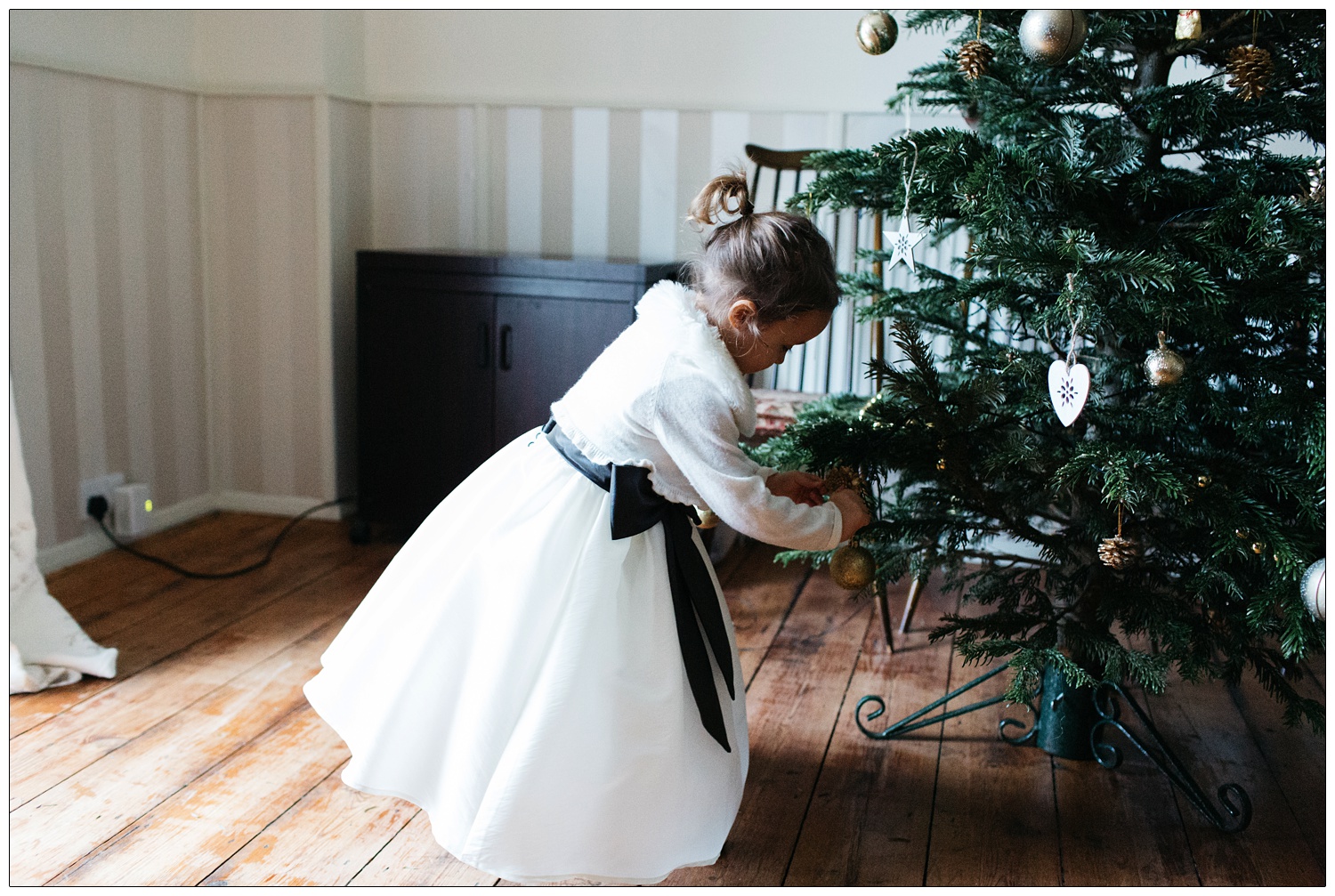 A little flower girl put s a bauble on a Christmas tree.