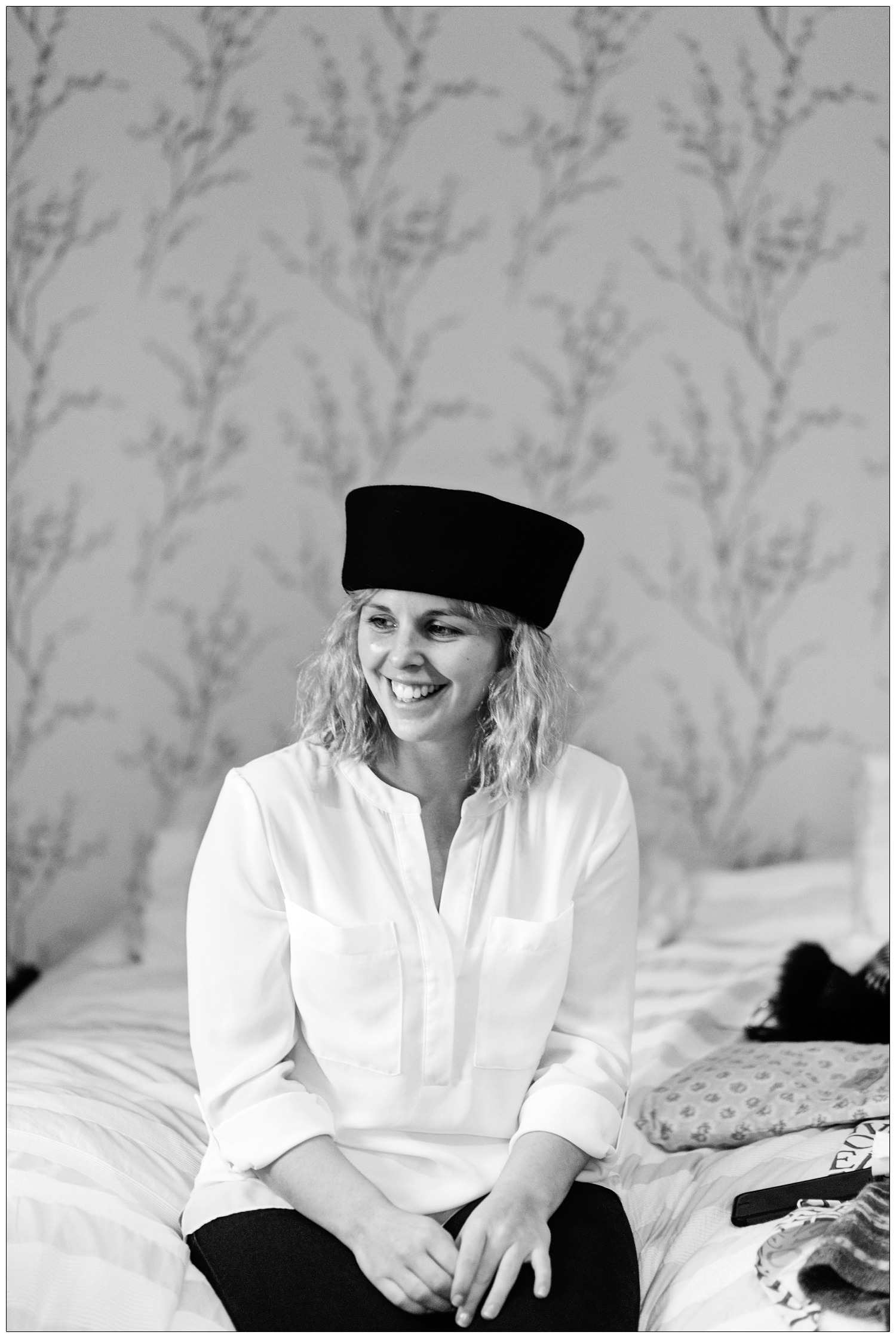 A woman sat on a bed wearing a big hat.