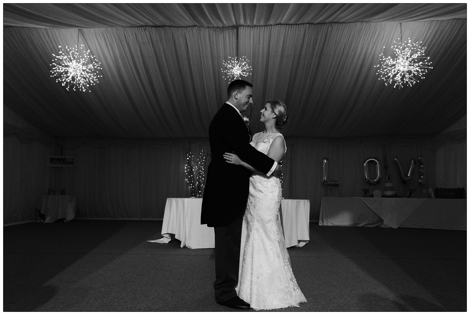 The bride and groom stand together, there are balloons that say love.