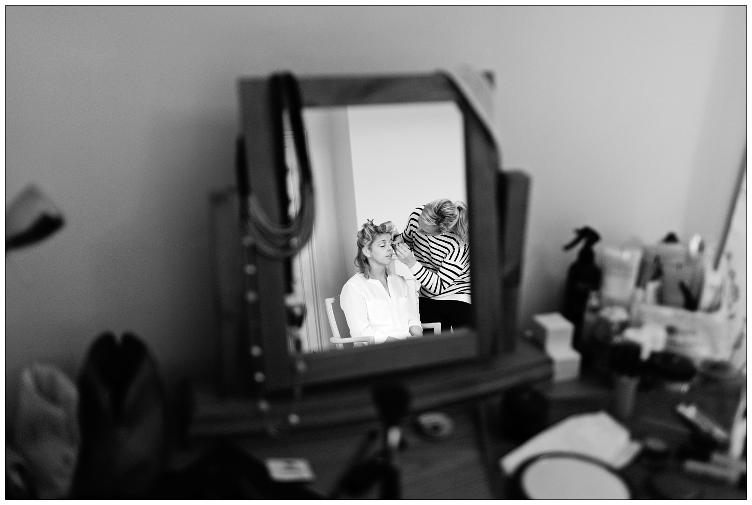 The bride having her makeup done, seen in a mirror.