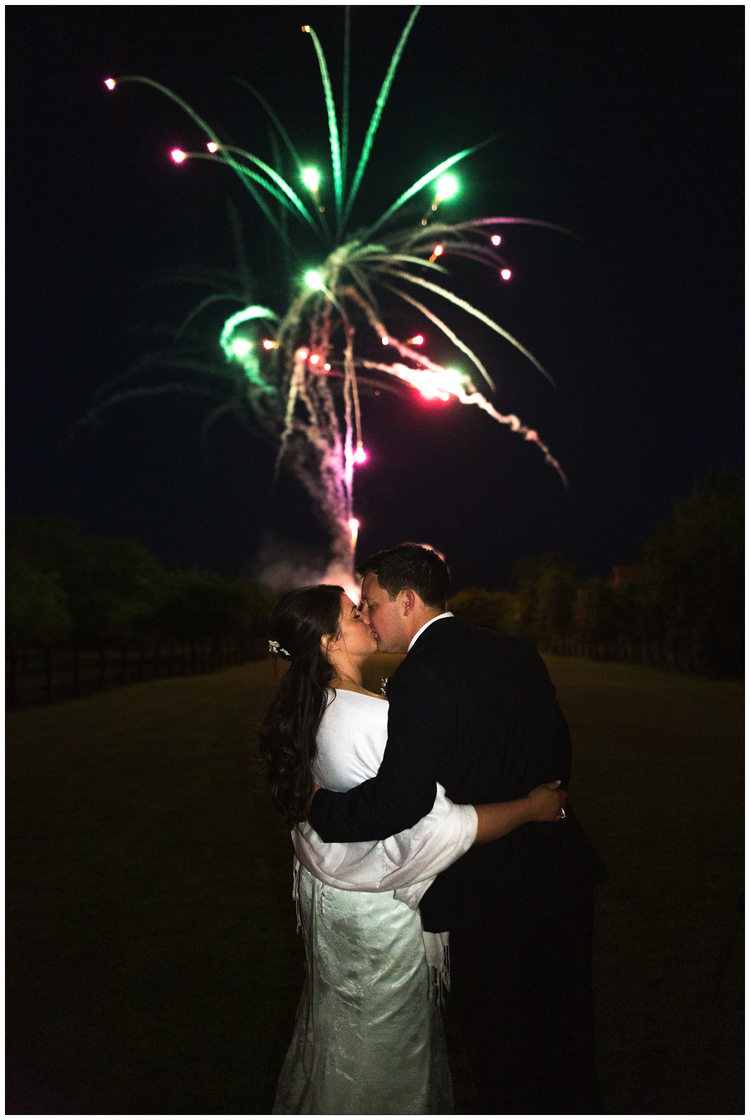bride and groom kissing in the garden in front of pink and green fireworks