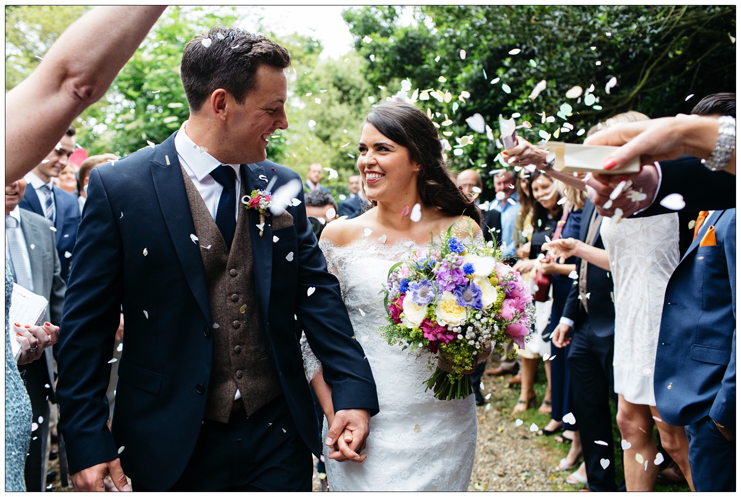 bride and groom walking through confetti and laughing in Purleigh Essex