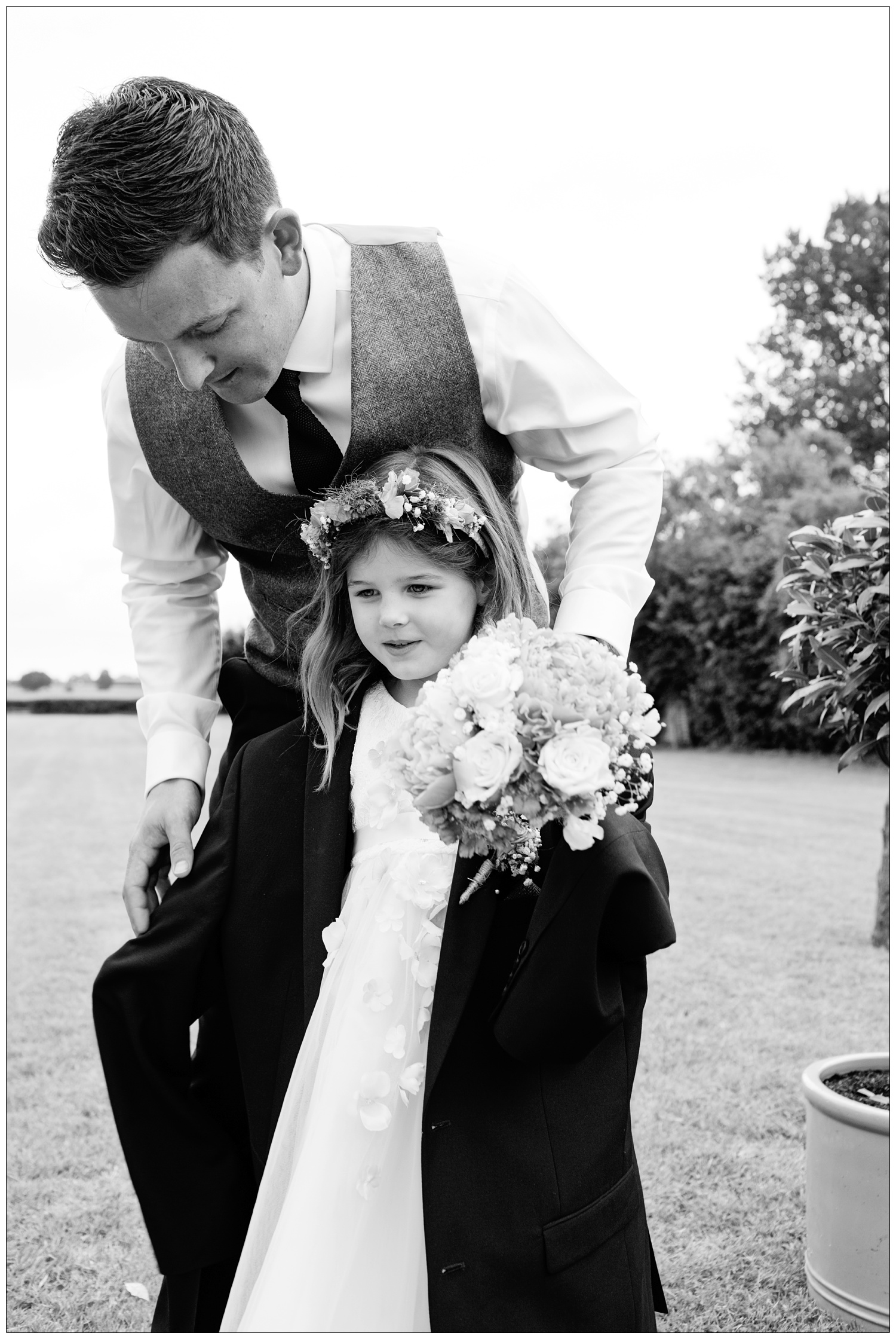 groom putting a man's jacket on a young flowergirl