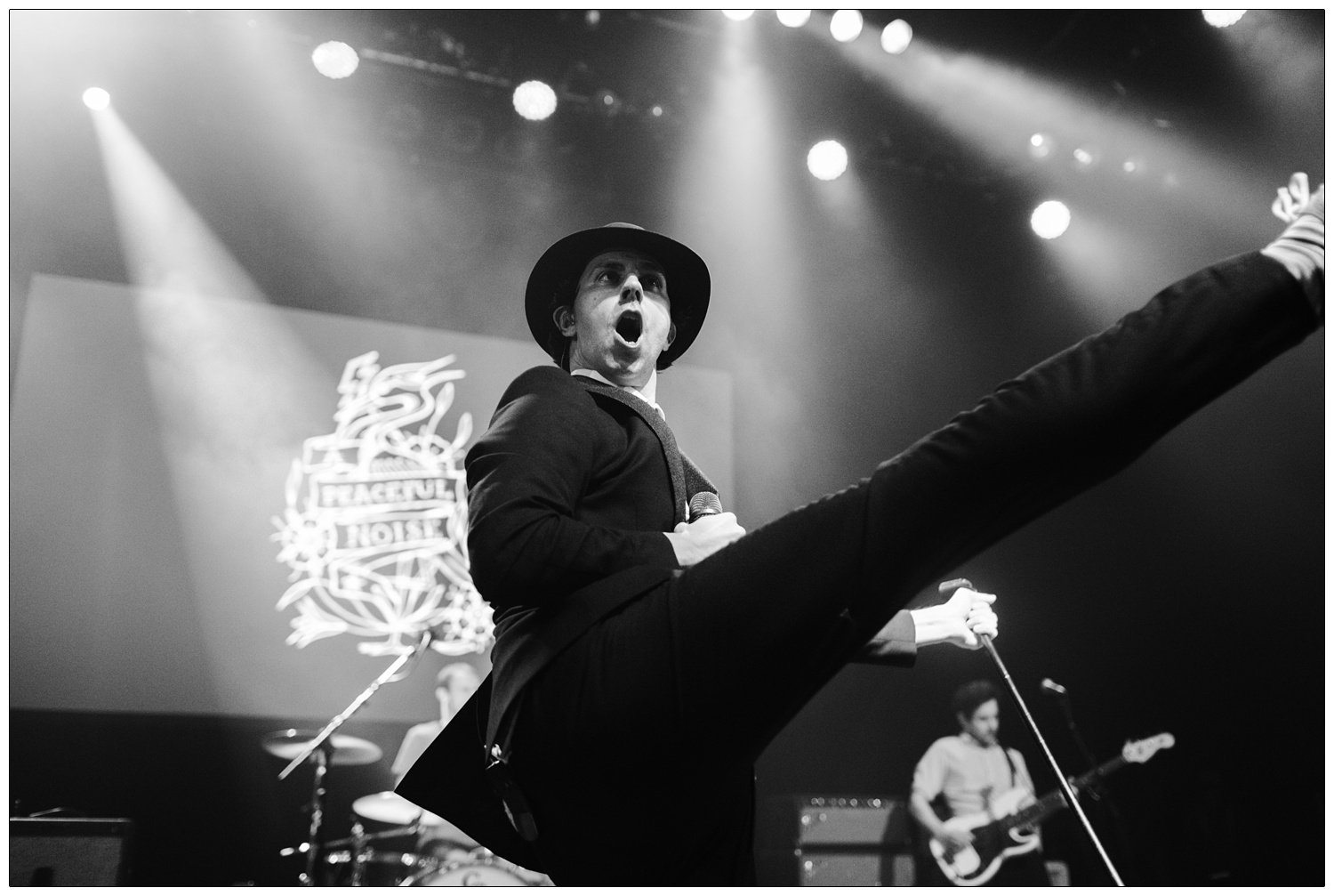 Black and white photograph of Paul Smith of Maxïmo Park kicking his leg in the air