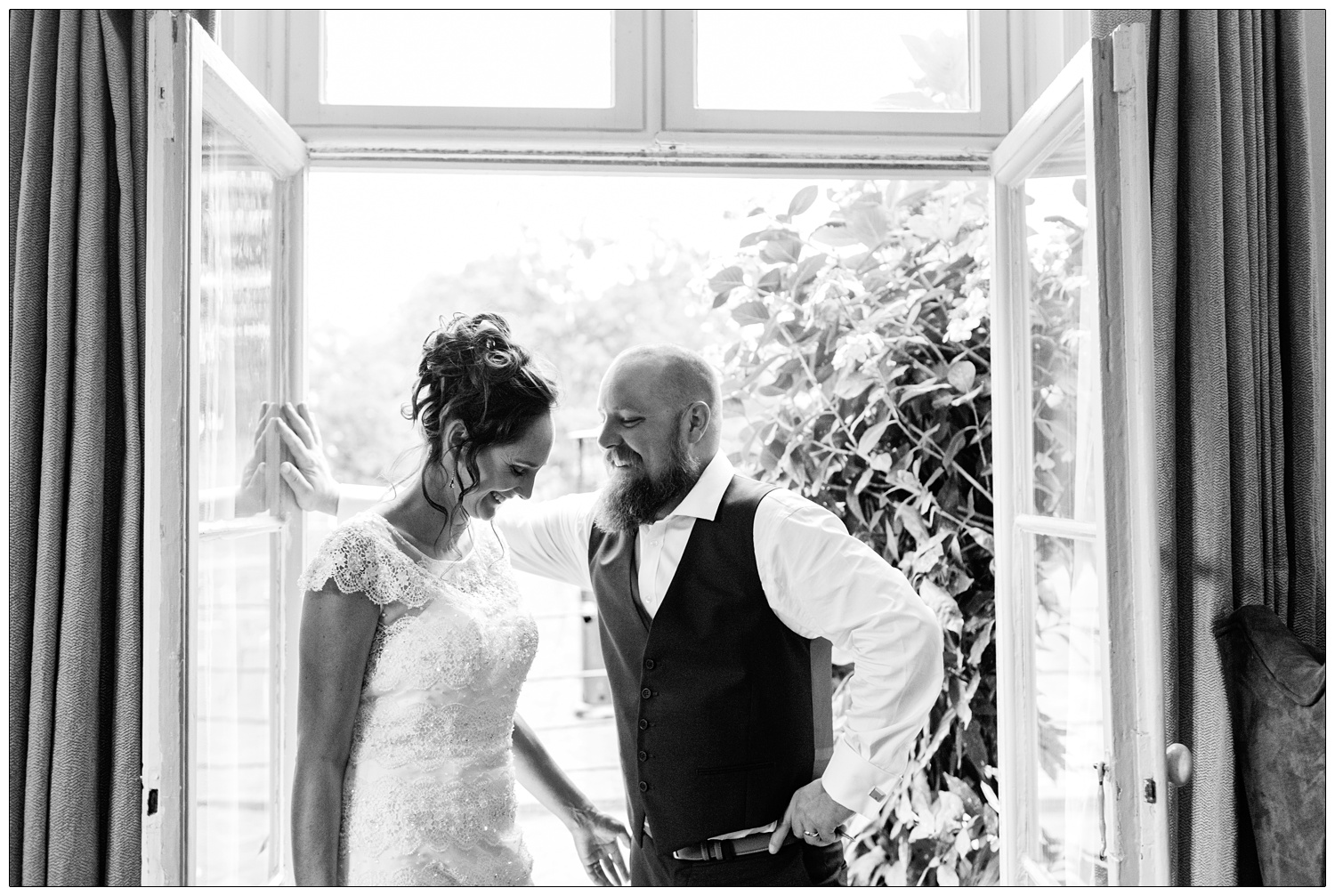 bride and groom laughing in a doorway in Maison Talbooth hotel, in a black and white photograph
