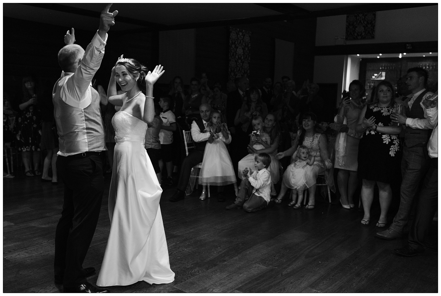 black and white photograph of bride and groom during first dance putting their hands in the air