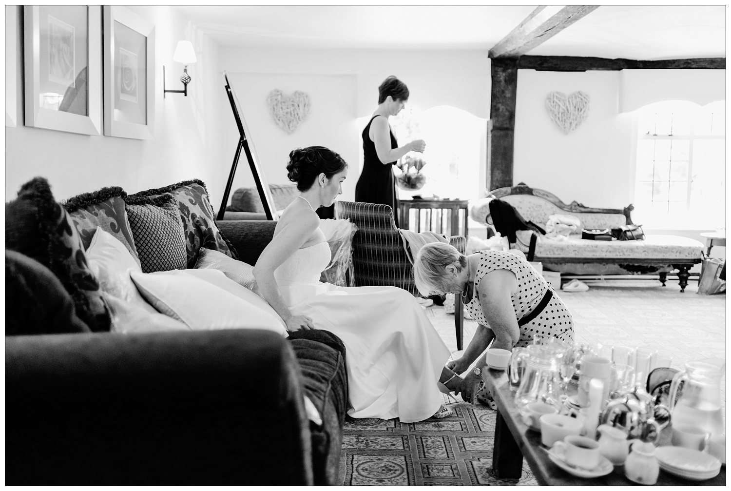 Bride having help with her shoes in a black and white photograph