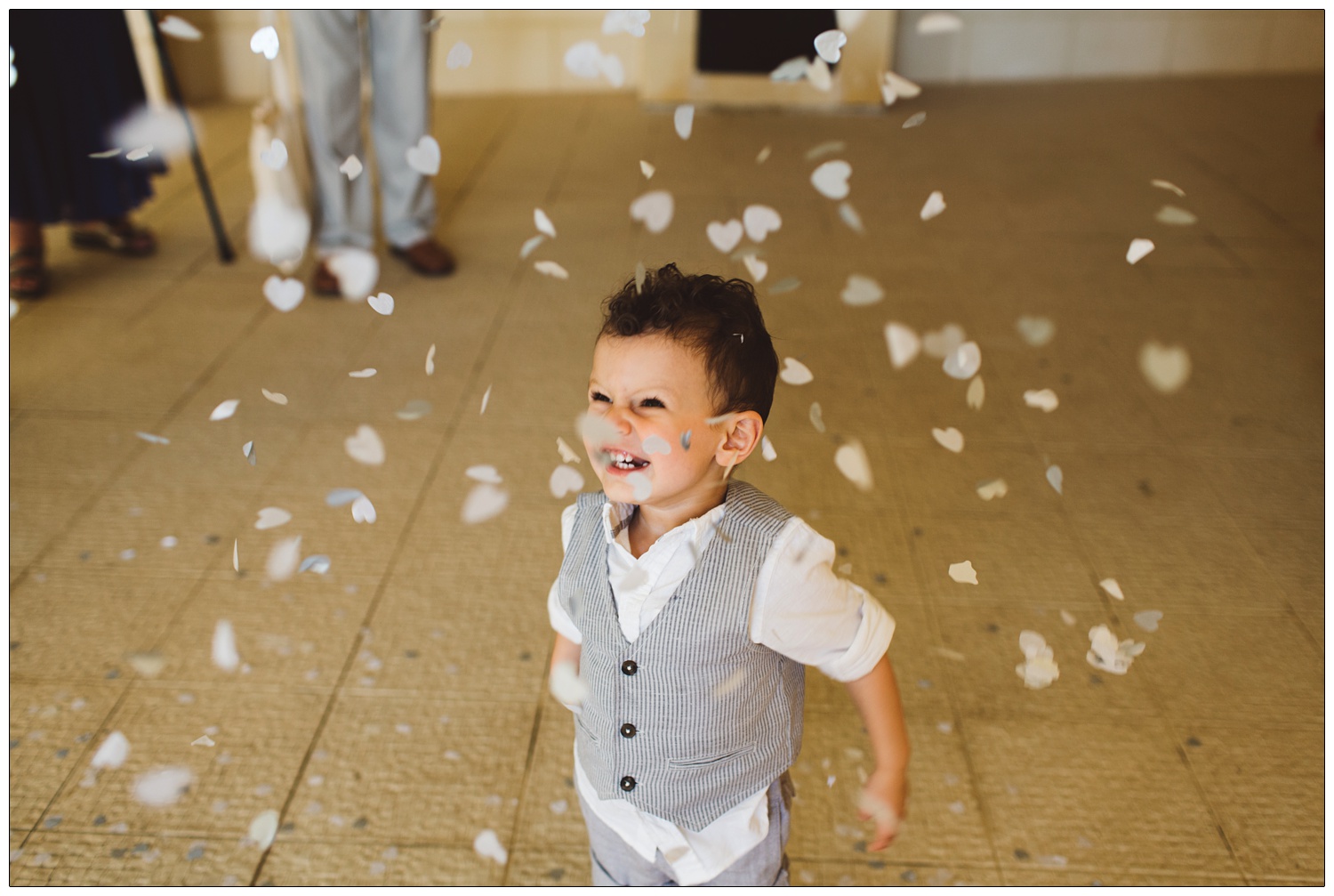little boy in a waistcoat throwing confetti over himself