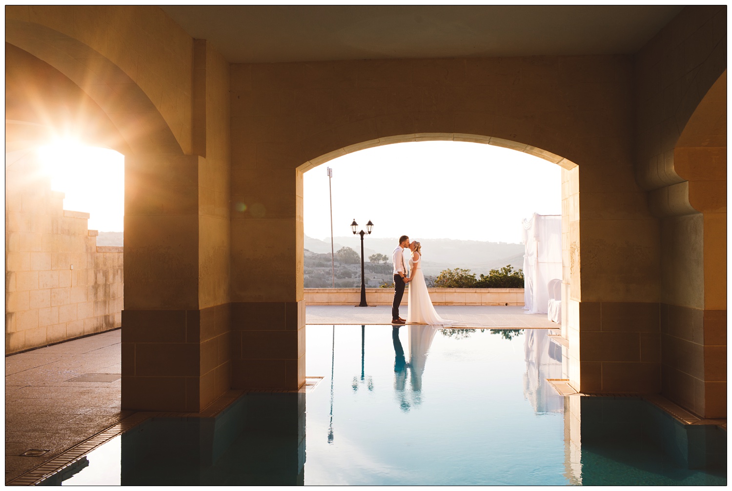 newly wed couple kissing by the pool at The Cornucopia Hotel with the sunflaring