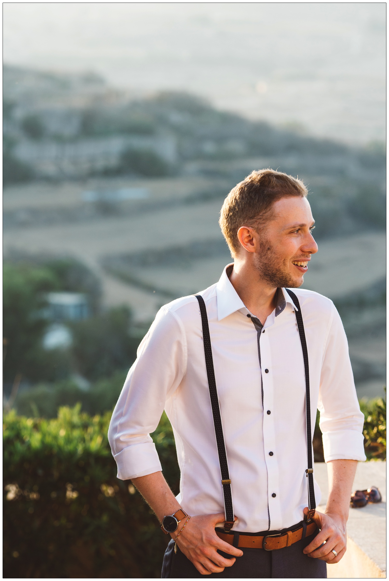 groom holding on to his braces in front of the Gozo landscape