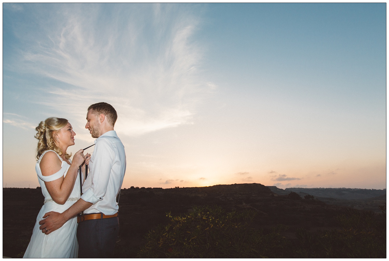 Bride holding the braces of her new husband as the sun sets.