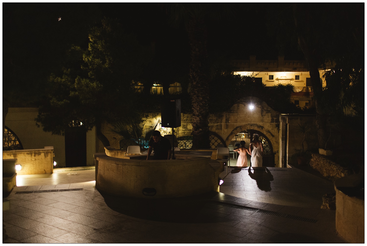 bride and bridesmaid walking down some steps in the light and a DJ in the shadow at his decks at a hotel in Gozo