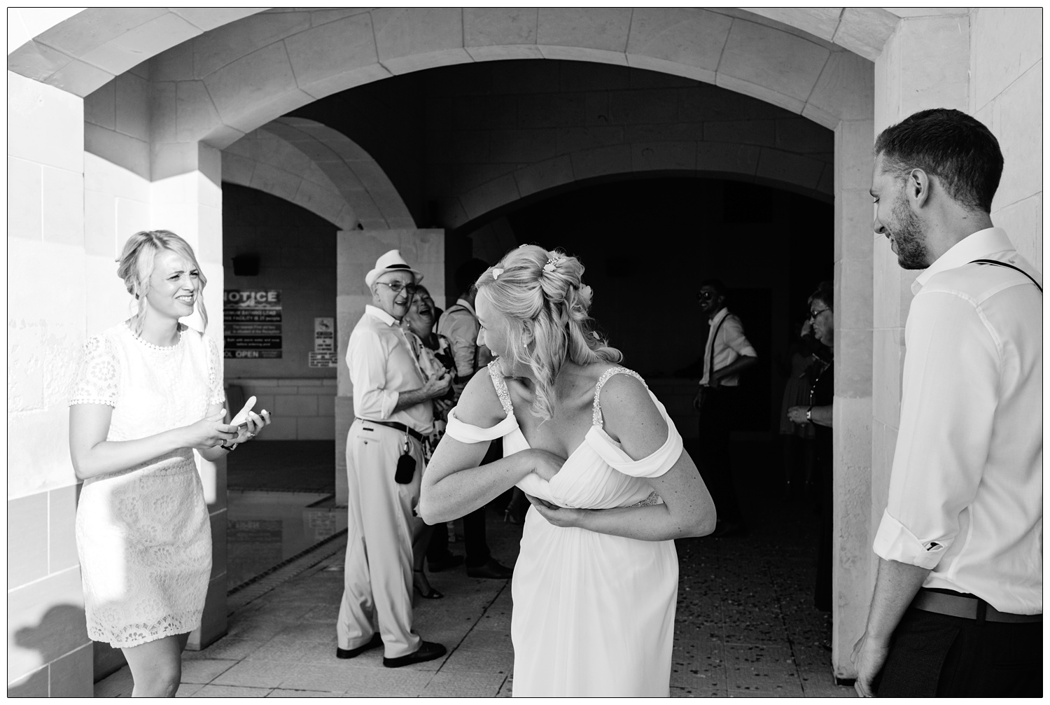 black and white candid moment of bride retrieving confetti out of her dress