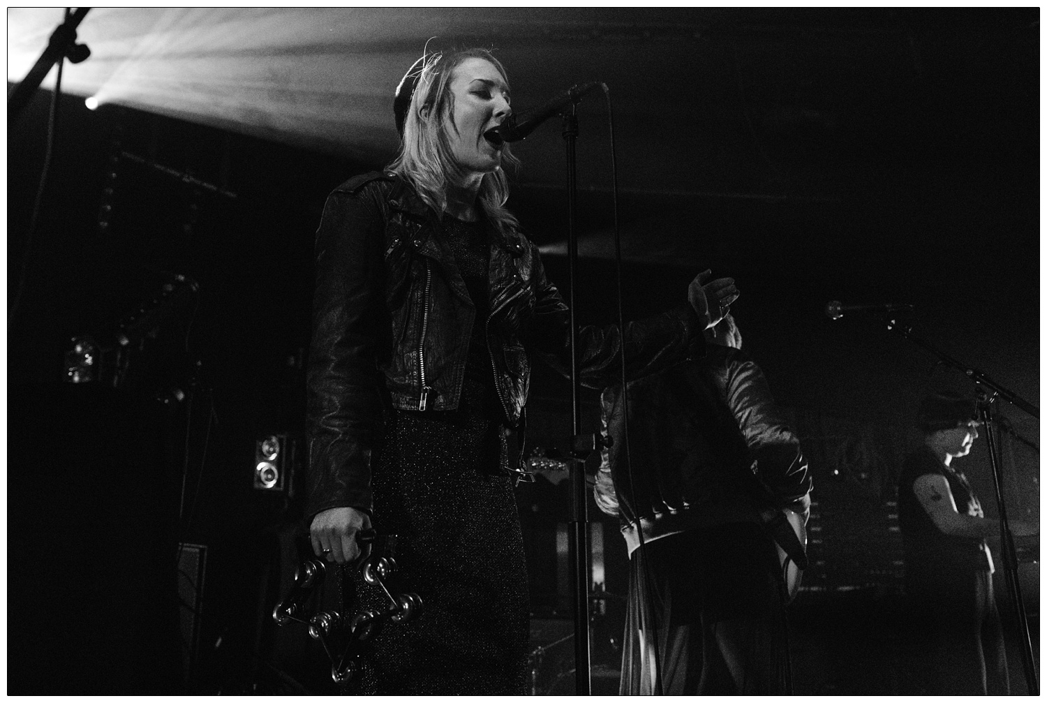 Faith Vern holding a tambourine and singing on stage with band PINS. Kyoko Swan on the keyboard.