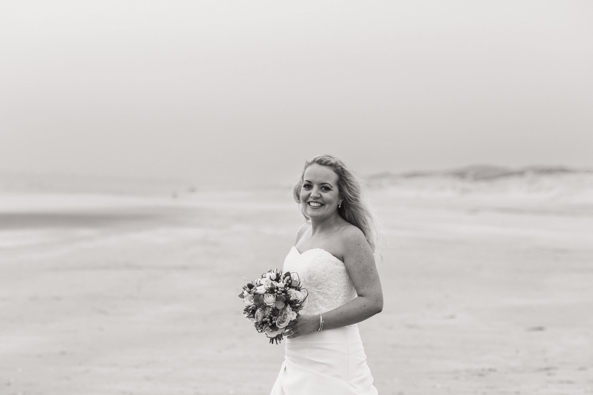 A bride holding flowers on the beach at Camber Sands. The Gallivant wedding.