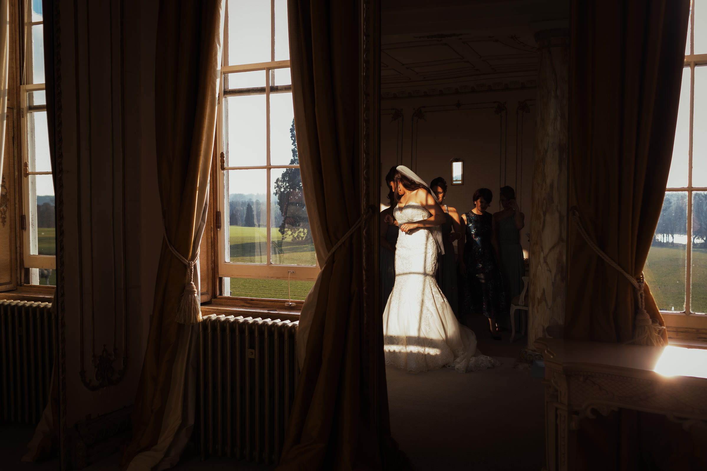 In the Rococo suite at Gosfield Hall. A reflection in a mirror of a bride in a fishtail wedding dress. Style 2713 by Mori Lee Madeline Gardner. The shadow of the window frame lands on her dress. Outside the windows you can see grass and trees. It's a sunny winter day.