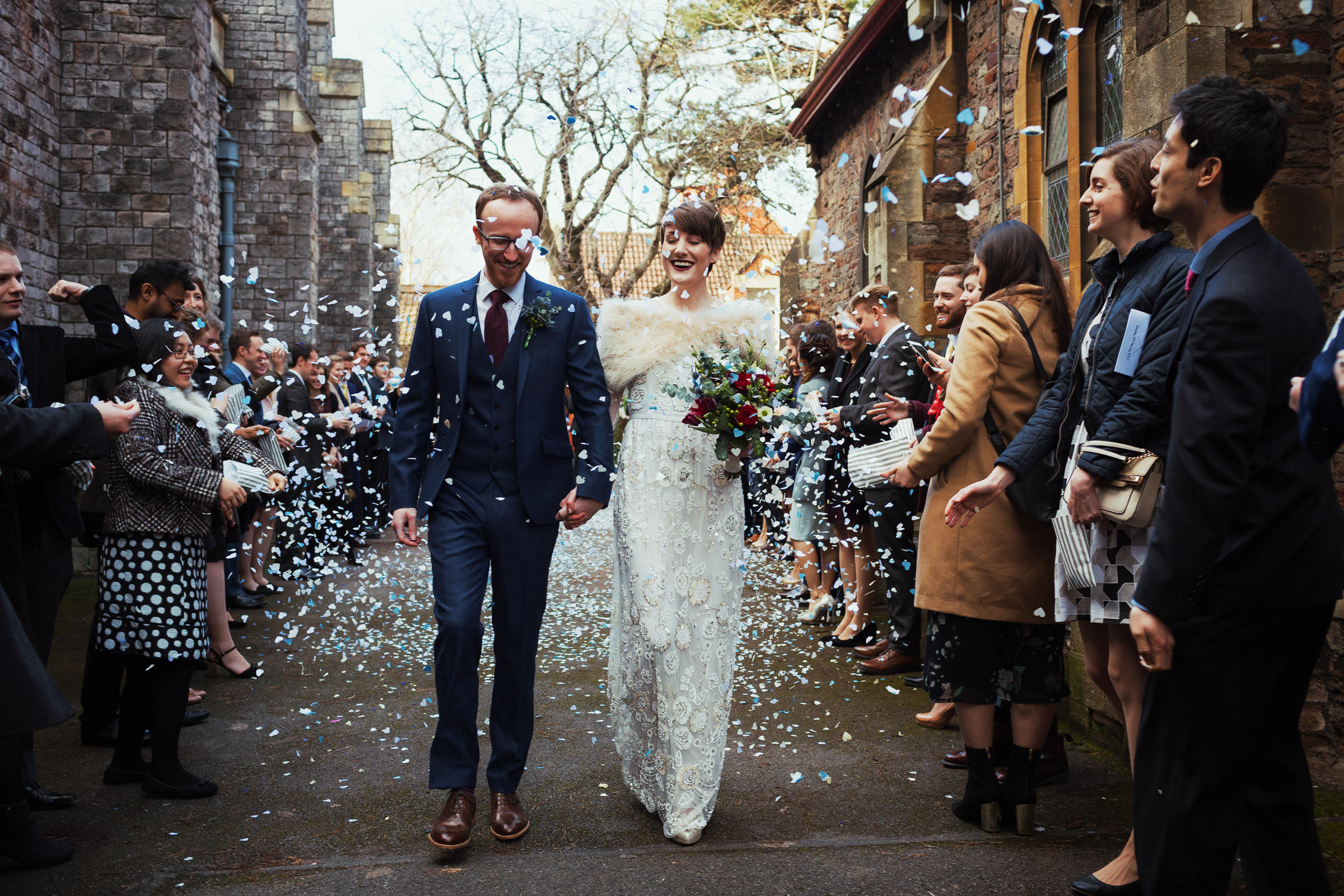 Confetti hearts falling on a man and woman after their wedding ceremony at St Alban's Church of Westbury Park Bristol wedding. The guests are wearing coats.