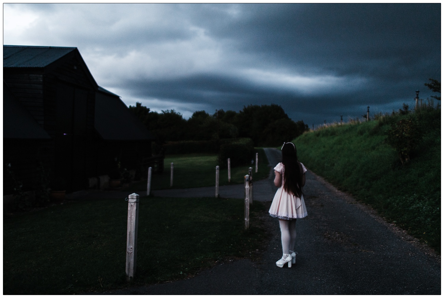 A woman with long dark hair is dressed in a Japanese street style fashion. A doll style dress with a puffy petticoat underneath. It is dark and she is outside the Alpheton Hall Barns wedding venue.