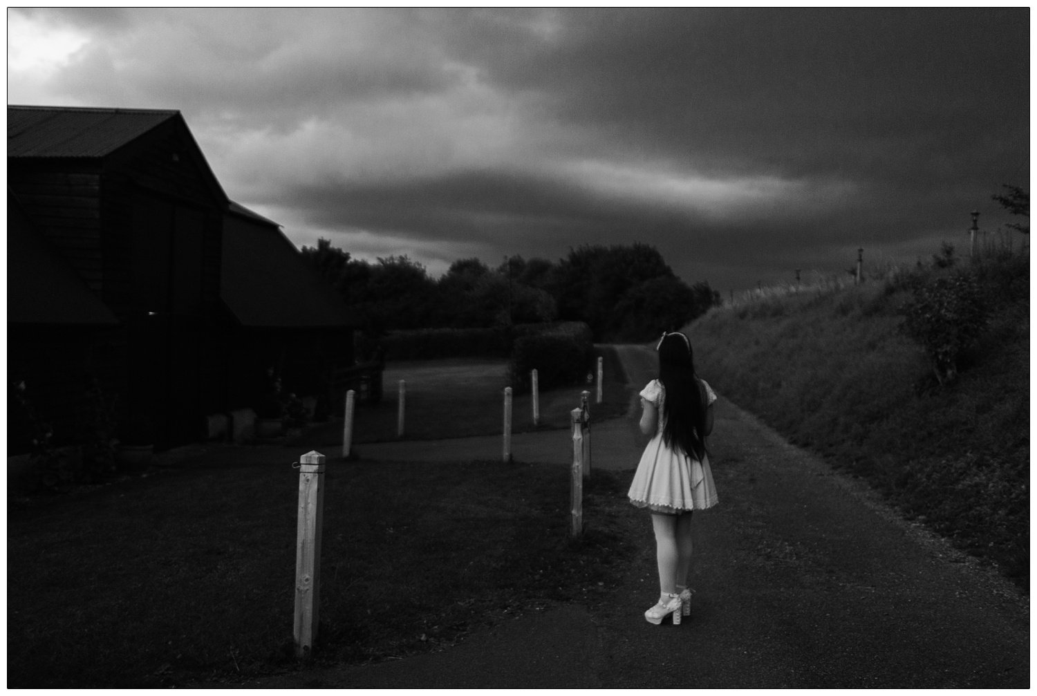 A woman with long dark hair is dressed in a Japanese street style fashion. A doll style dress with a puffy petticoat underneath. It is dark and she is outside the Alpheton Hall Barns venue.