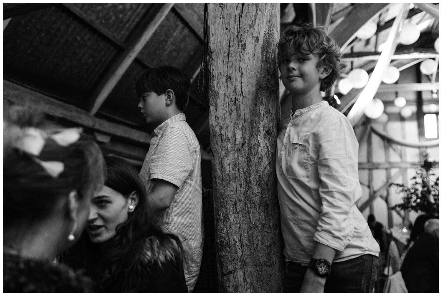A boy leaning against a wooden post in a barn. A natural moment at a wedding.