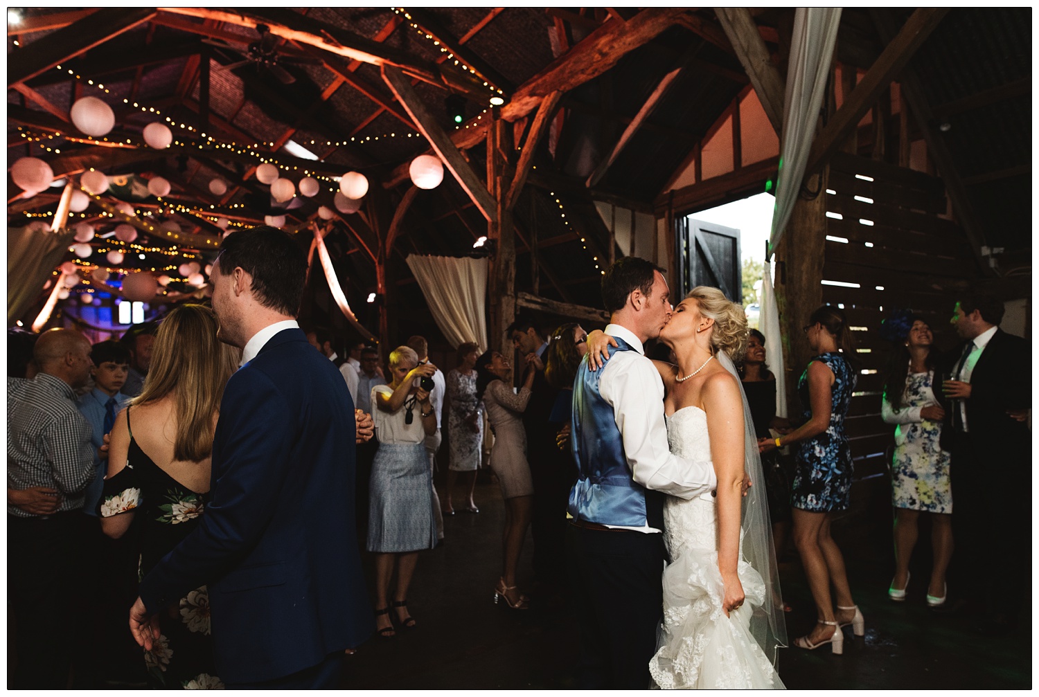 Bride and groom kissing on the dance floor surrounded by guests in Alpheton Hall Barns.