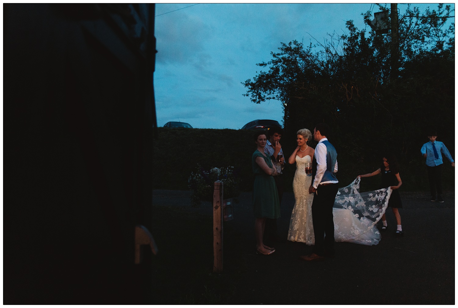 A girl plays with the back of the brides dress outside in the twilight.