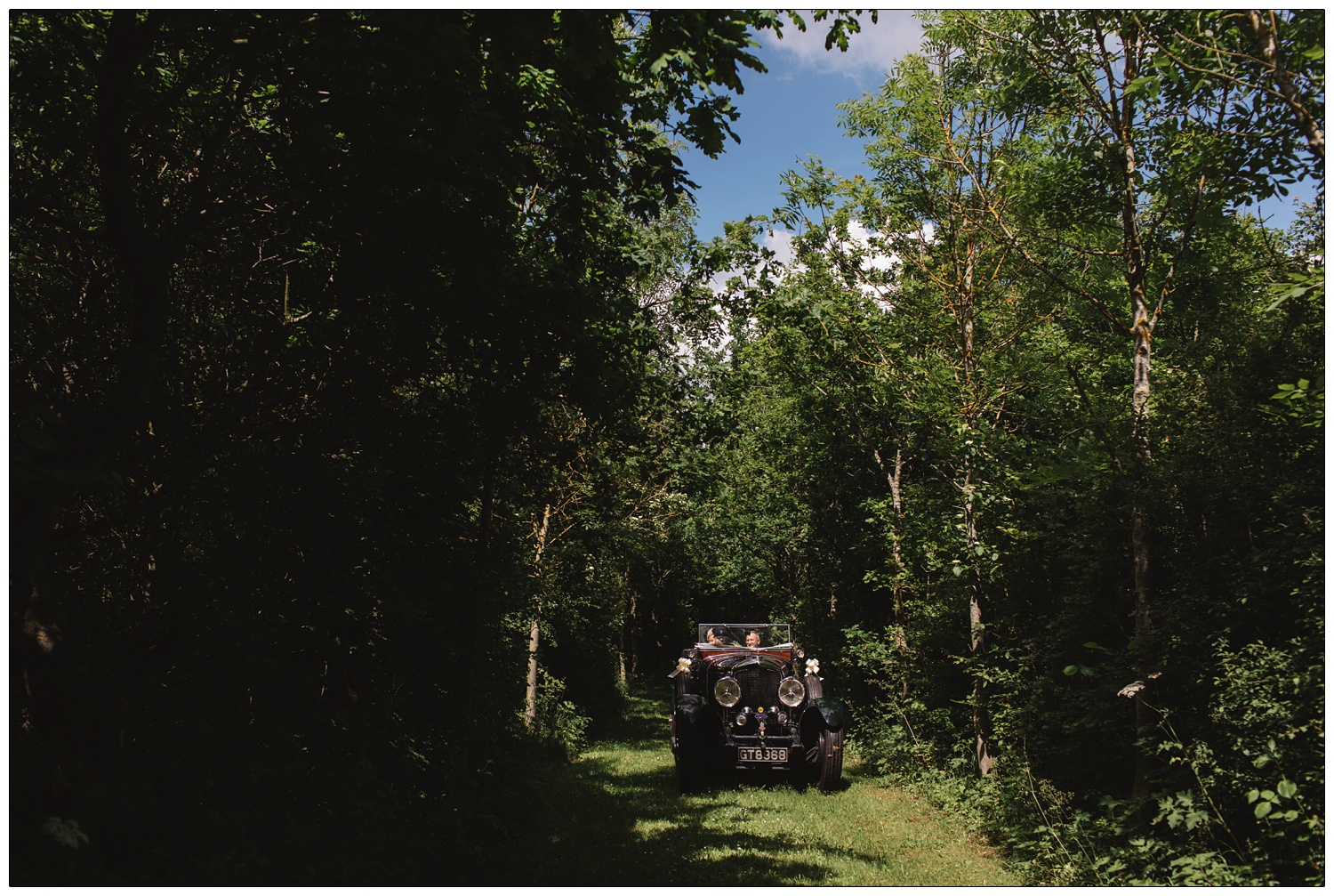 Bride arriving at Alpheton Hall Barns surrounded by trees in a 1931 green Bentley.