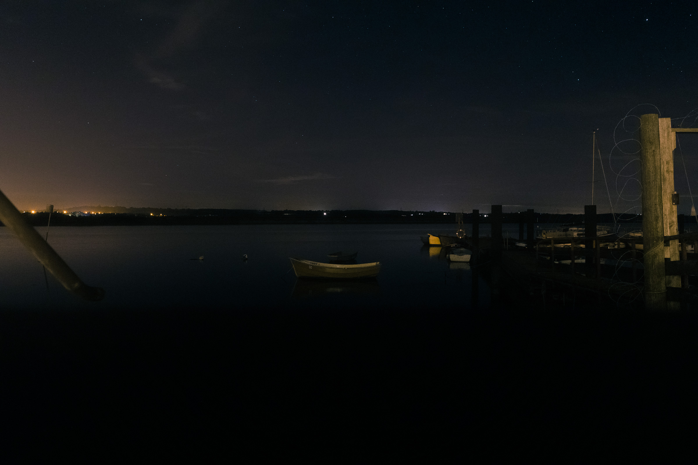 A boat on the River Crouch at night, outside the Brandy Hole in Hullbridge. You can see the stars in the sky and the glow of orange lights from South Woodham Ferrers across the river.