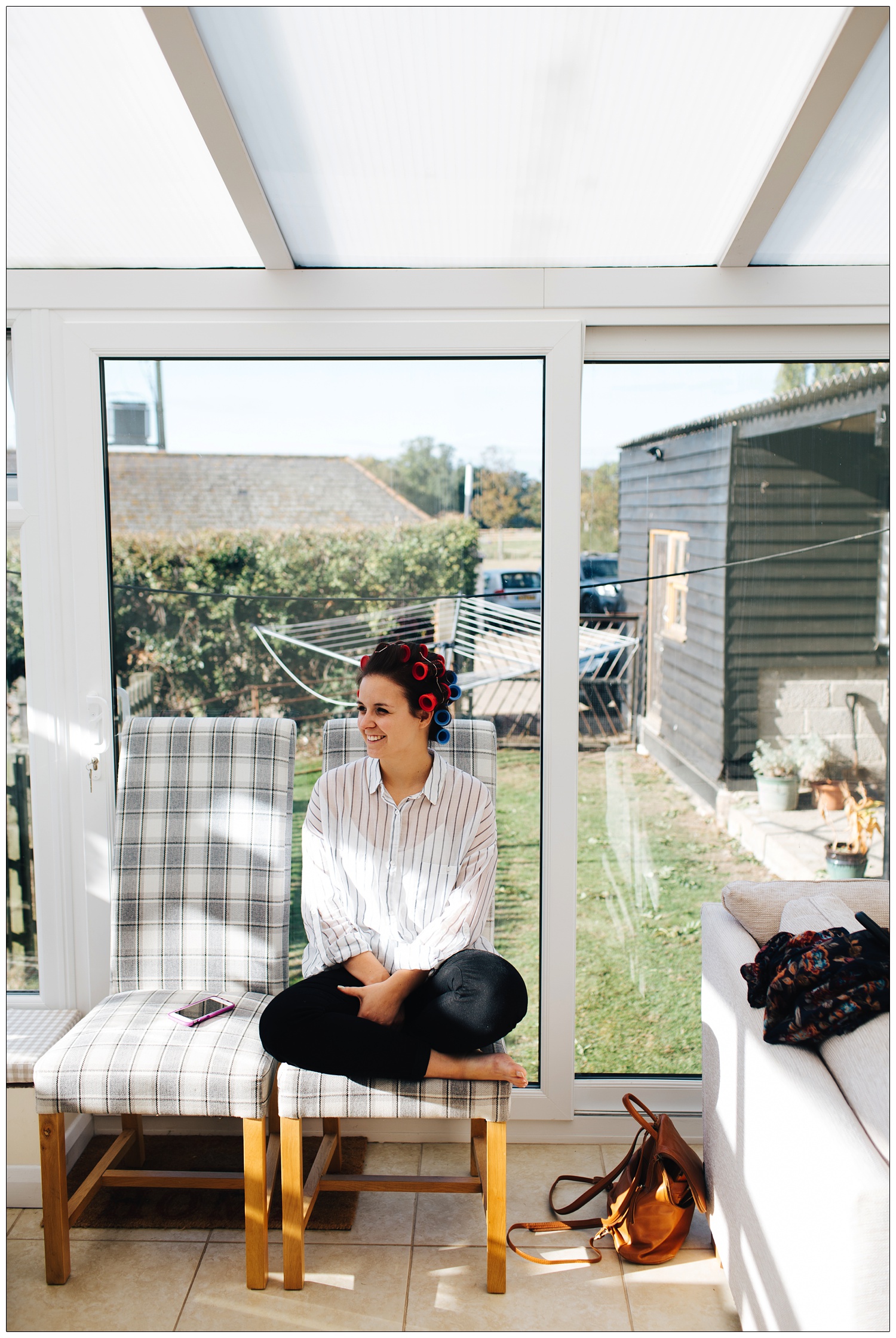 Woman sitting on a chair in a conservatory with rollers in her hair.