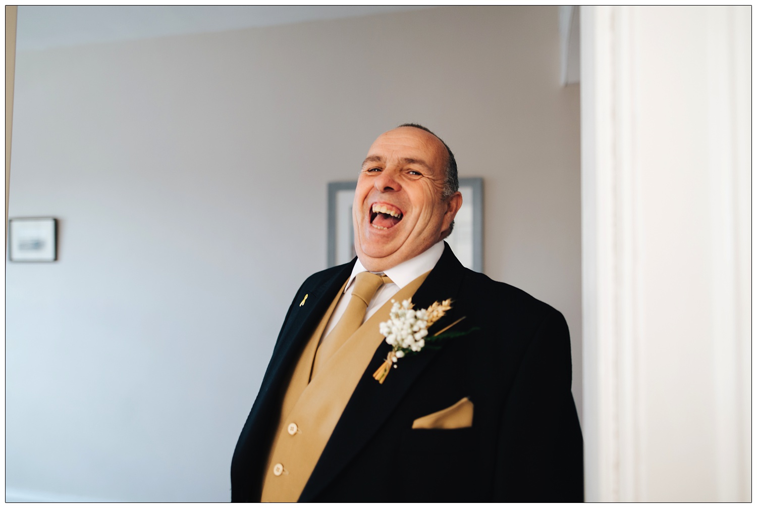 Father of the bride dressed in his suit laughing at the camera.