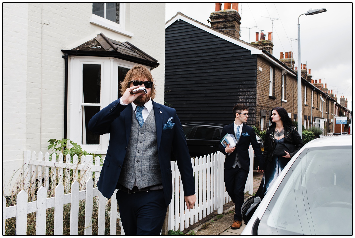 Man takes a drink from a hip flask as he walks along the street to a wedding in Maldon. Two guests are behind him.