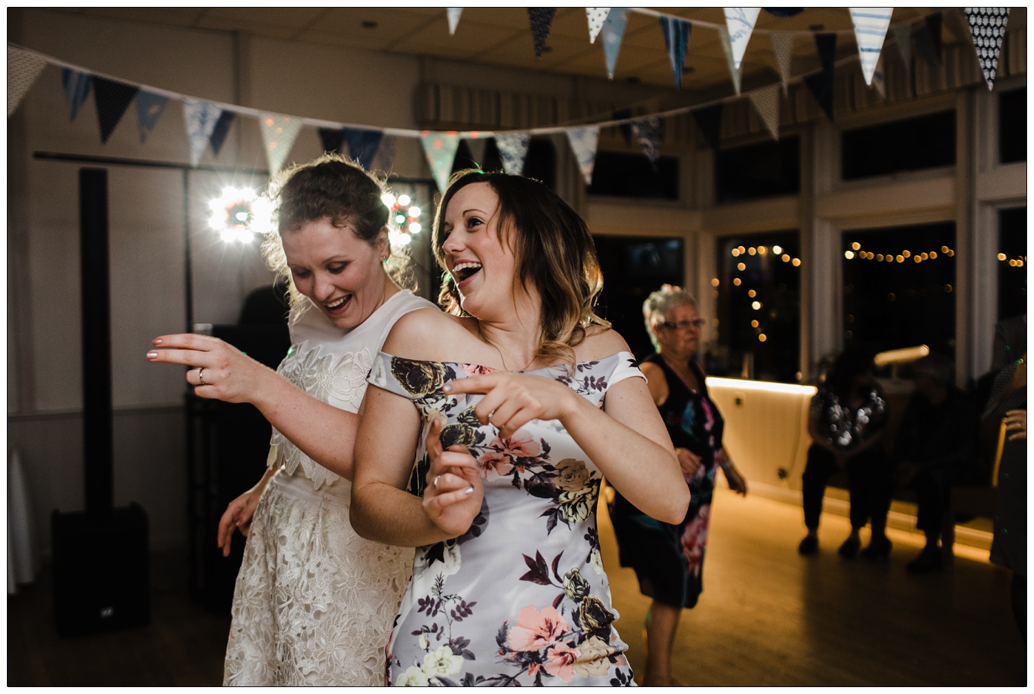 Bride dancing with her friend. There is bunting on the ceiling.