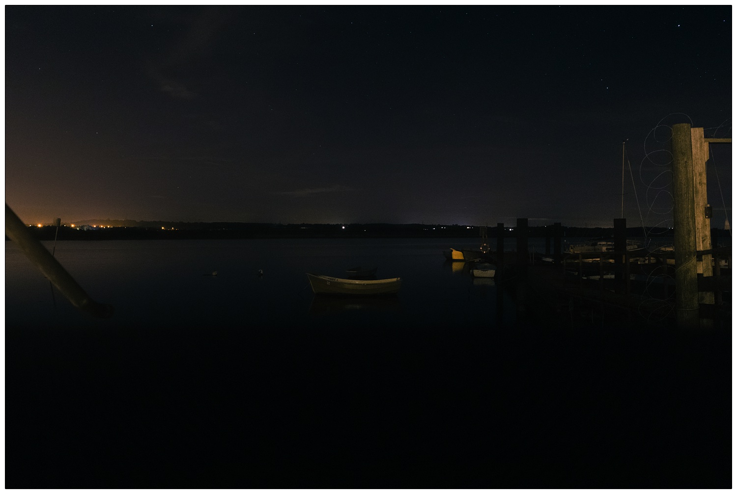 A boat on the River Crouch at night, outside the Brandy Hole in Hullbridge. You can see the stars in the sky and the glow of orange lights from South Woodham Ferrers across the river.
