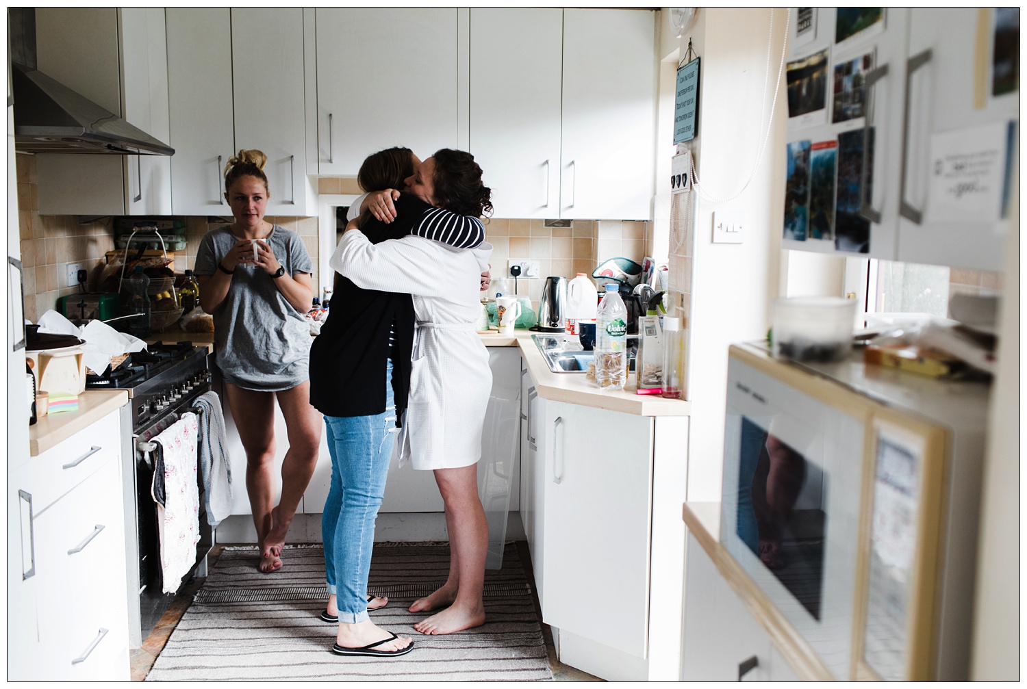 Women in a kitchen on the morning of a wedding. The bride hugs another woman.