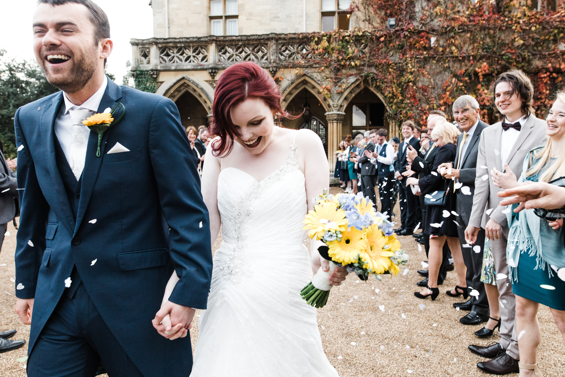 At Manor by the Lake wedding venue, a black and white photograph of man and woman holding hands. They just walked through a tunnel of guests throwing confetti.