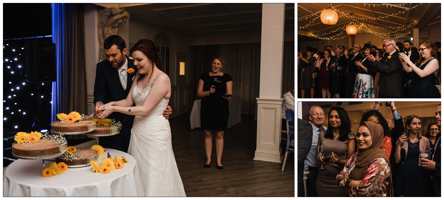 People watch the newly married couple cut the cake which is decorated with yellow gerbera daisies.