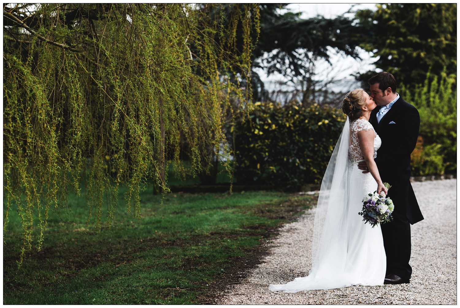 Bride and groom are kissing. The bride is holding flowers by her side.