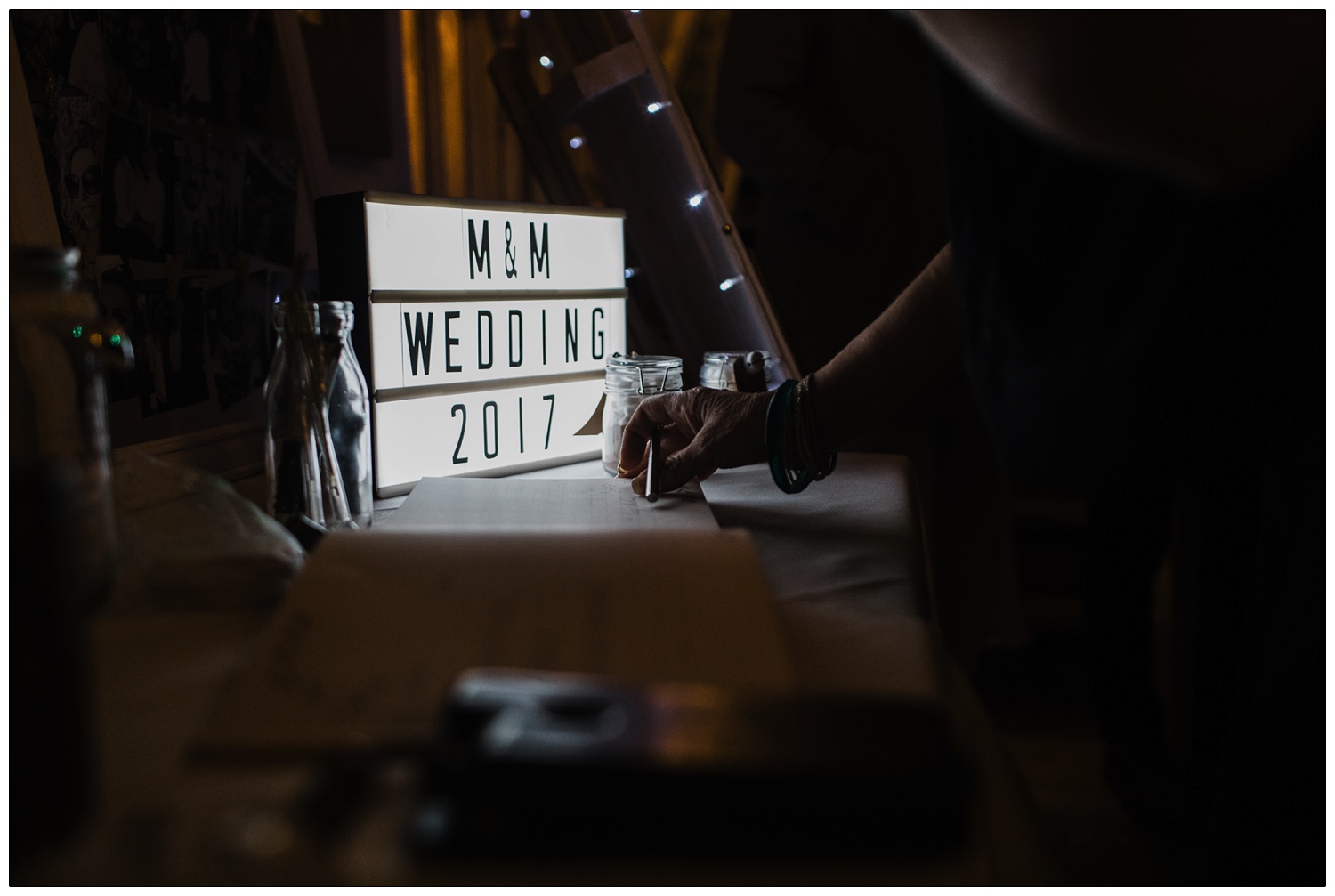 A cinema light box that says "M&M Wedding 2017". Someone is signing the guestbook in front of the light.