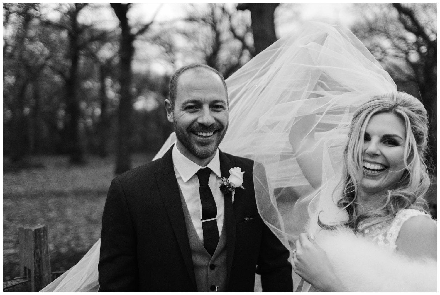 Bride and groom in a black and white photograph in Hockley woods in December. The wind is blowing the brides veil.