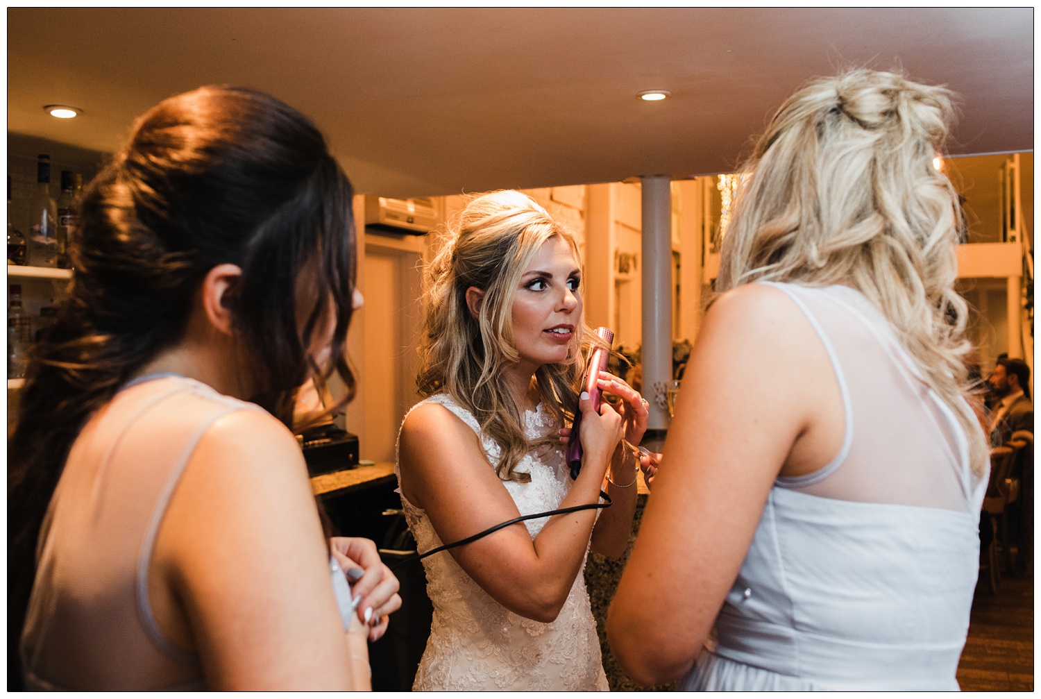 Bride is curling her hair with pink straighteners in the bar area.