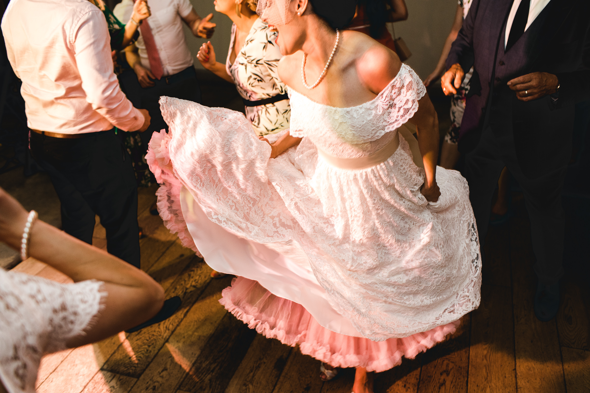 The bride dressed in a vintage style off the shoulder lace dress is dancing. She is holding her dress and singing. She is in the Foundry at the Houchins wedding venue.