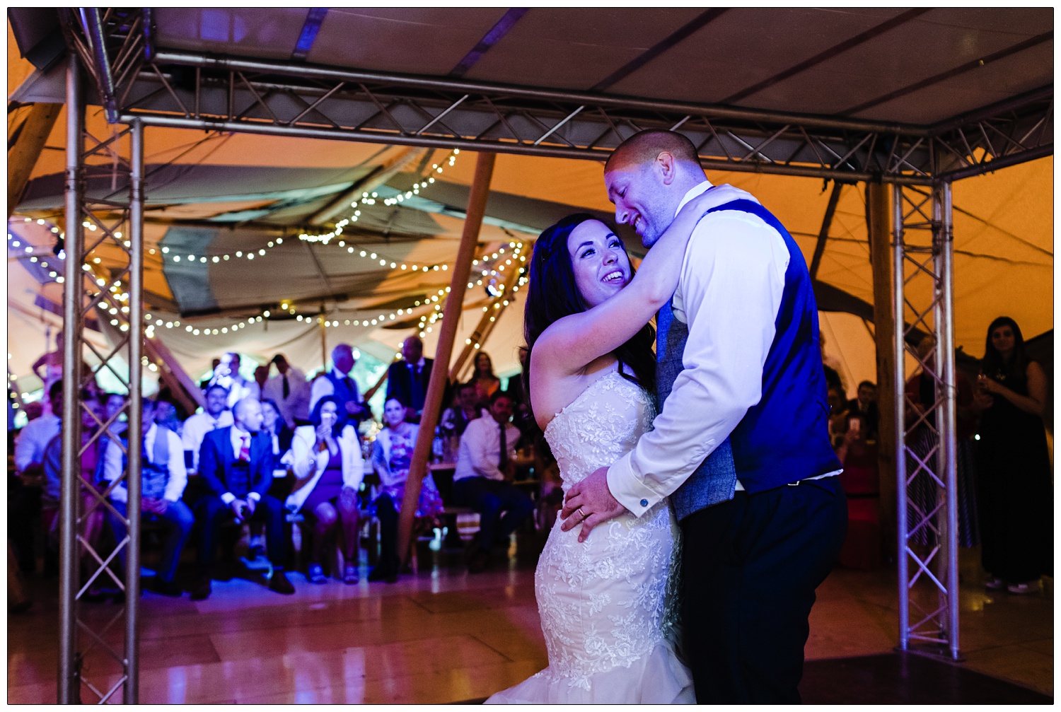 First dance under purple lights. The guests watch from the tables.