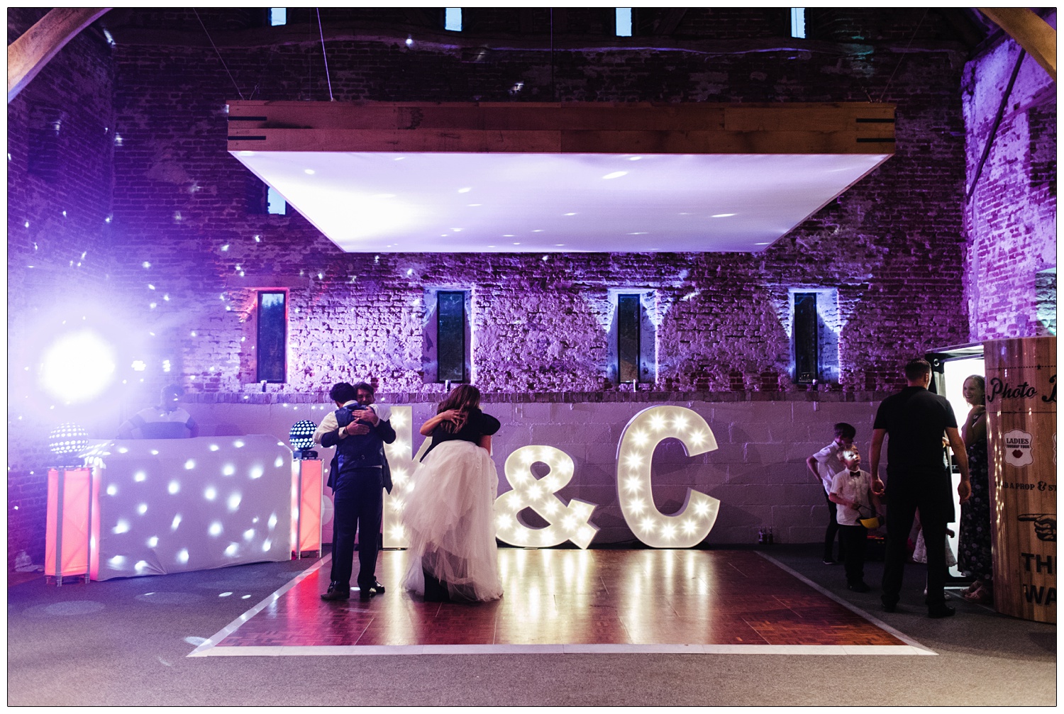 The dance floor lit with purple lights, the bride and groom are hugging friends.