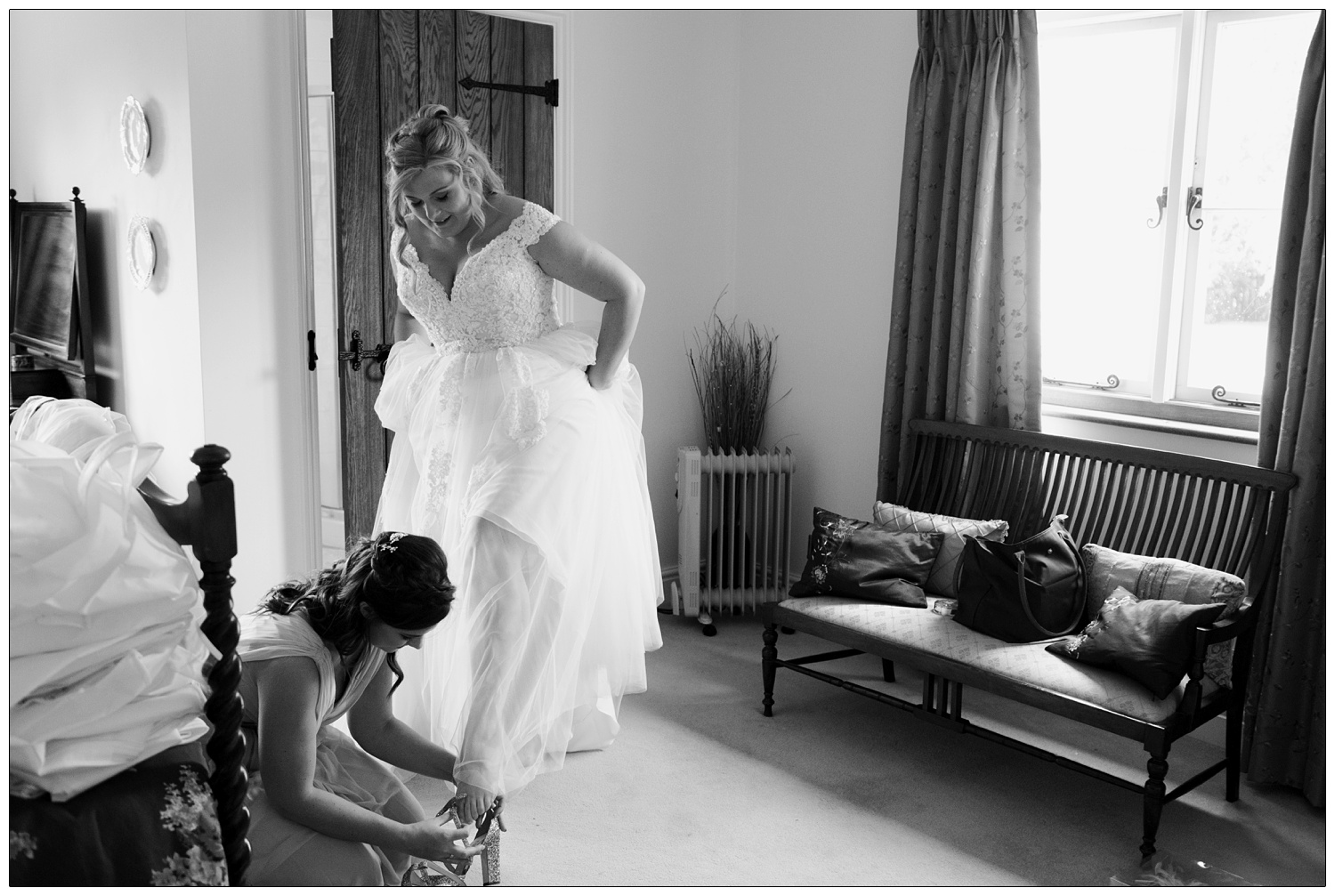 Bridesmaid putting on the bride's shoes in a bedroom.