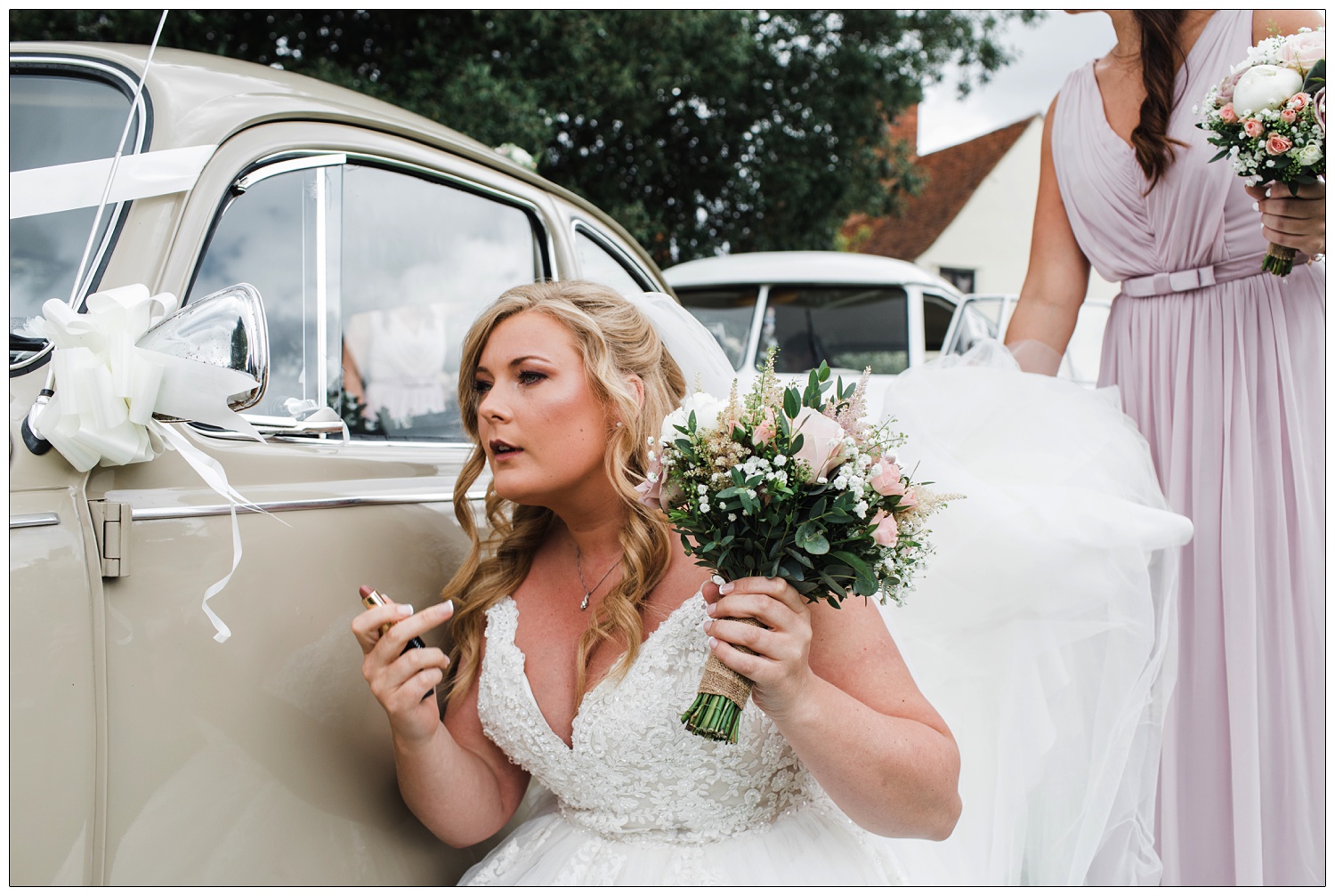 Bride checking her lipstick in the wing mirror of a beige 1968 Volkswagen Beetle.