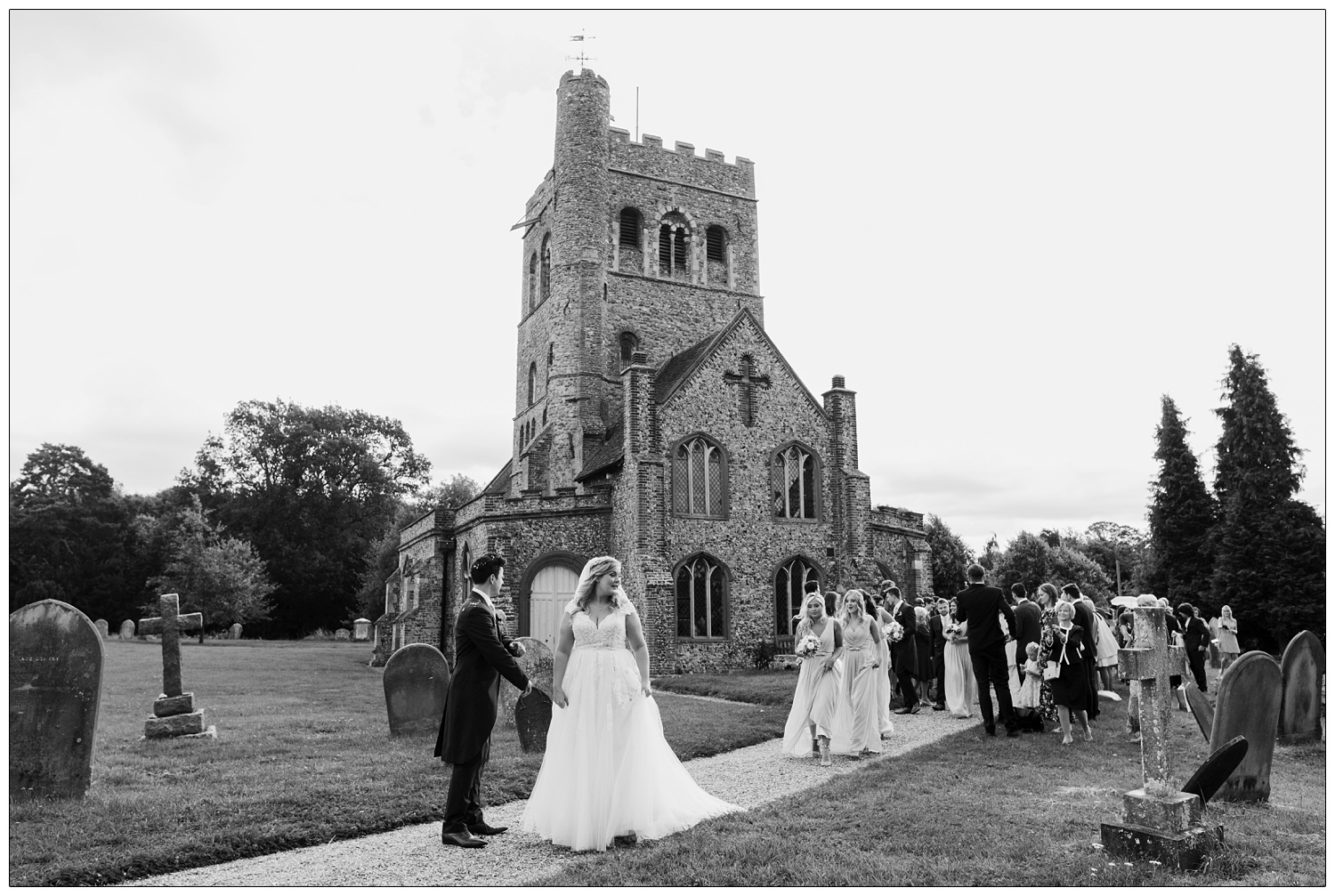 Black and white photograph of Bride and groom followed by the bridesmaids outside the St Barnabas church in Great Tey.